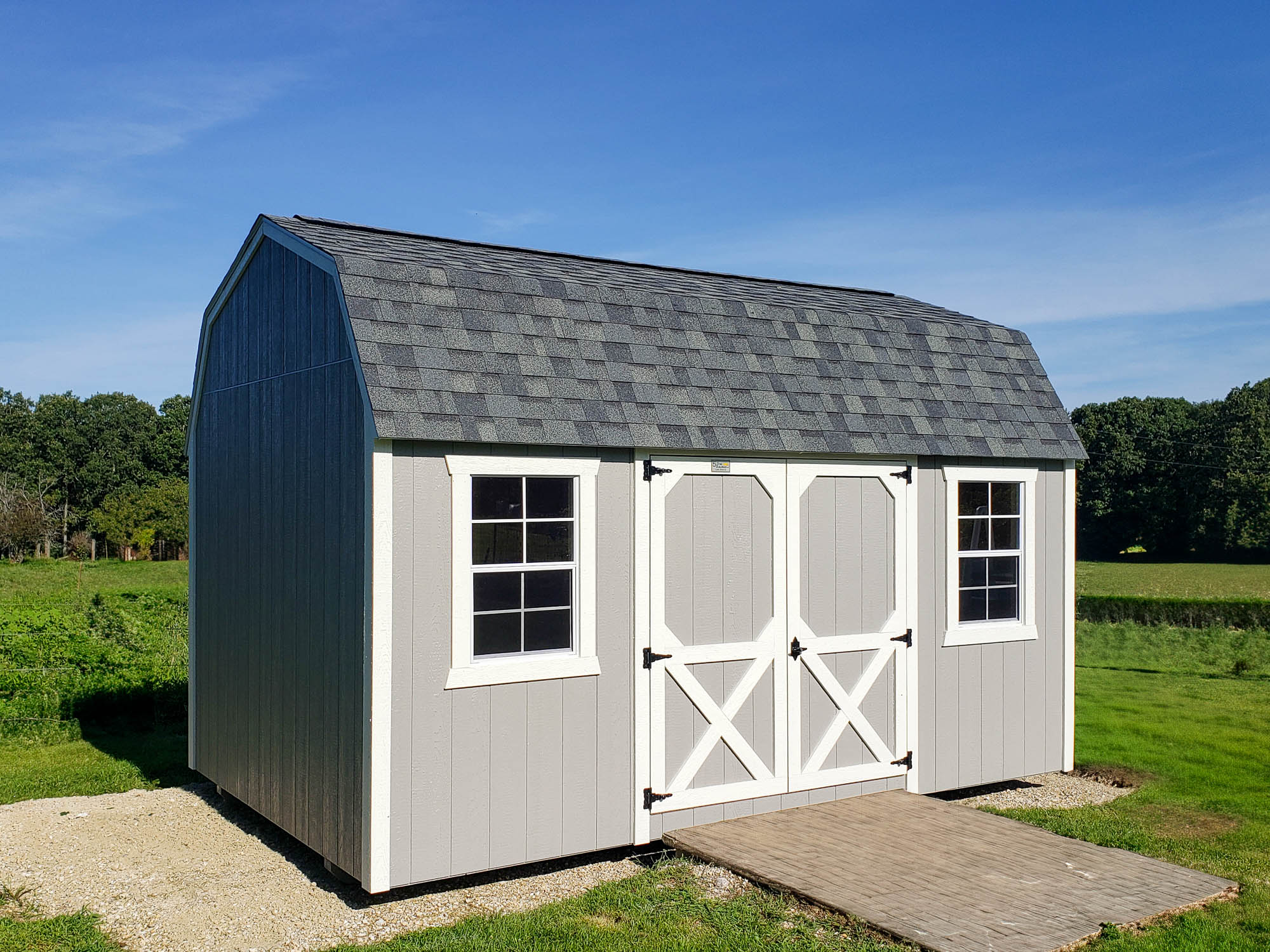 Lofted Barn Shed with gray siding, white trim, double doors, and two windows, placed on a concrete pad under a clear blue sky.